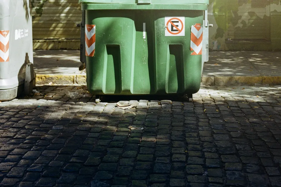 A green commercial waste container on a cobblestone street